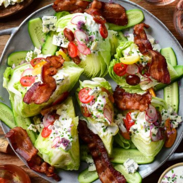 A large wedge salad with six lettuce wedges topped with dressing, tomatoes and pieces of bacon.