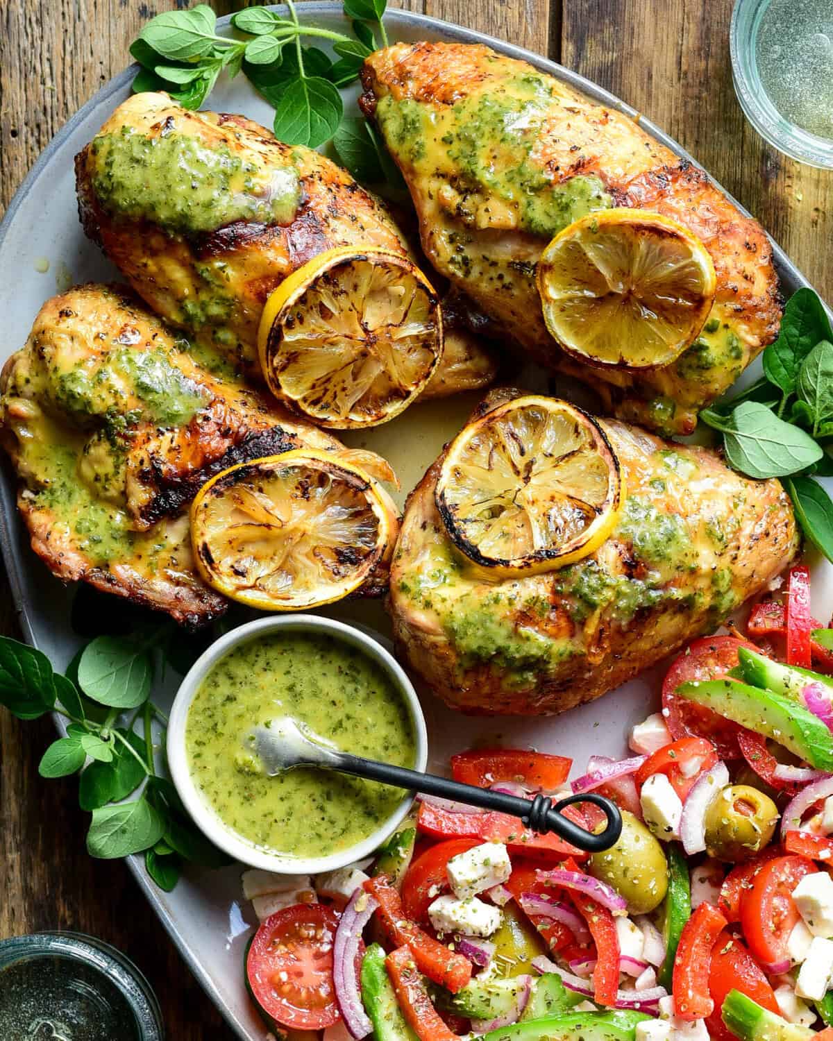 Four grilled and charred chicken breasts with charred lemon slices and served with a tomato salad. 