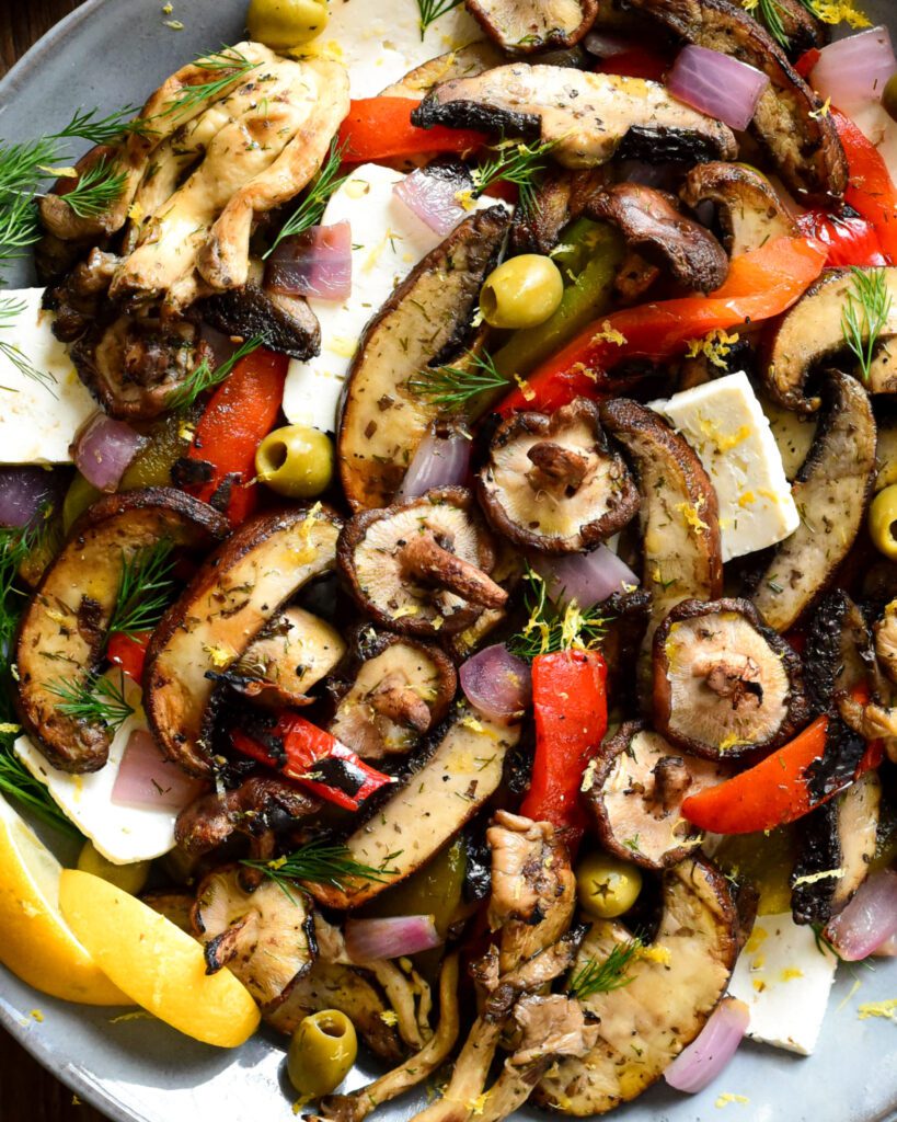 A close up of a round platter of Mediterranean Grilled Mushroom Salad with peppers, olives and feta cheese.