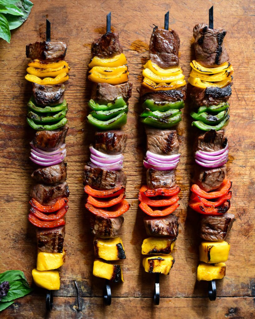 Four grilled beef skewers with alternating pieces of mango, peppers and onions.