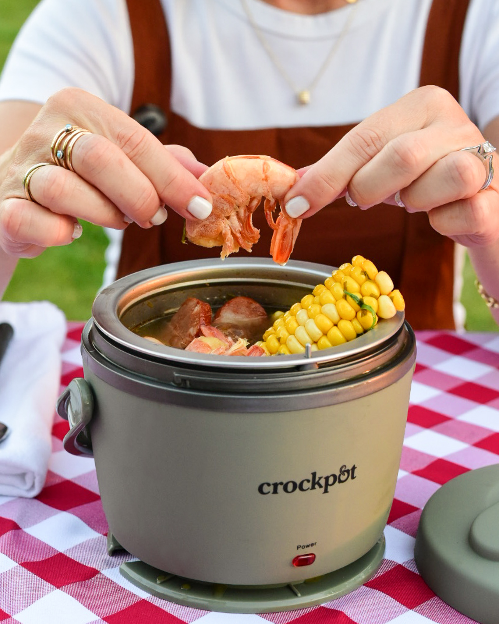 A close up image of a lunch crock Crockpot of a woman holding a shrimp that she is about to eat from her shrimp boil meal.
