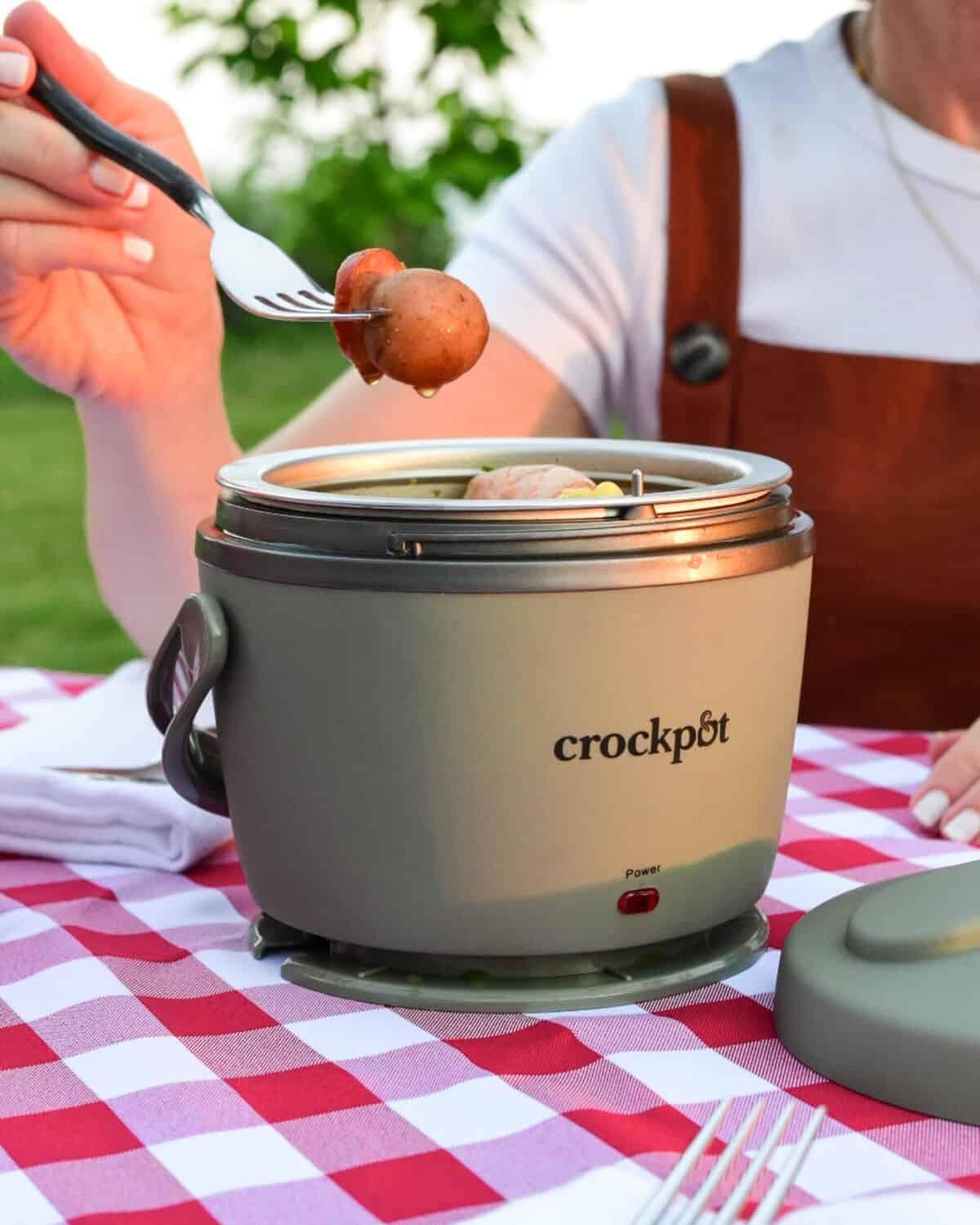A close up image of a lunch crock Crockpot of a someone holding a fork with a potato on it and about to eat it.