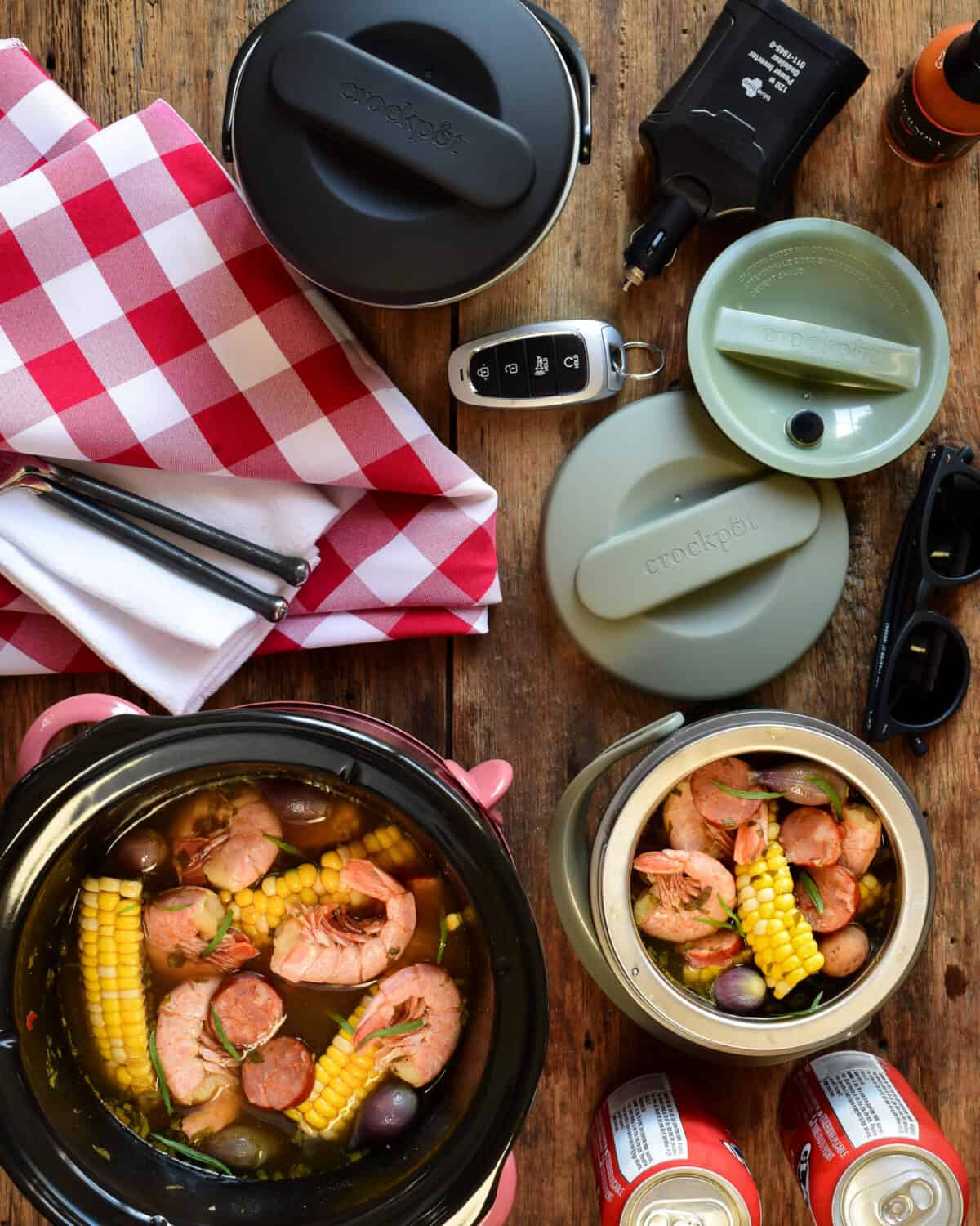 Three crockpots, a large on and two mini lunch crocks getting filled with a shrimp boil. A red and white tablecloth, keys, a car charger and sunglasses are the table as well.