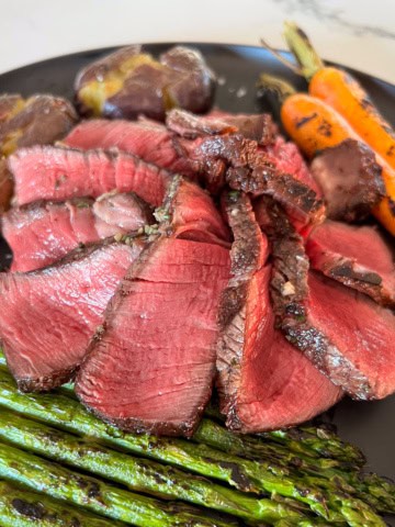 A perfectly cooked filet Mignon slices and fanned on a plate with asparagus, carrots and potatoes.