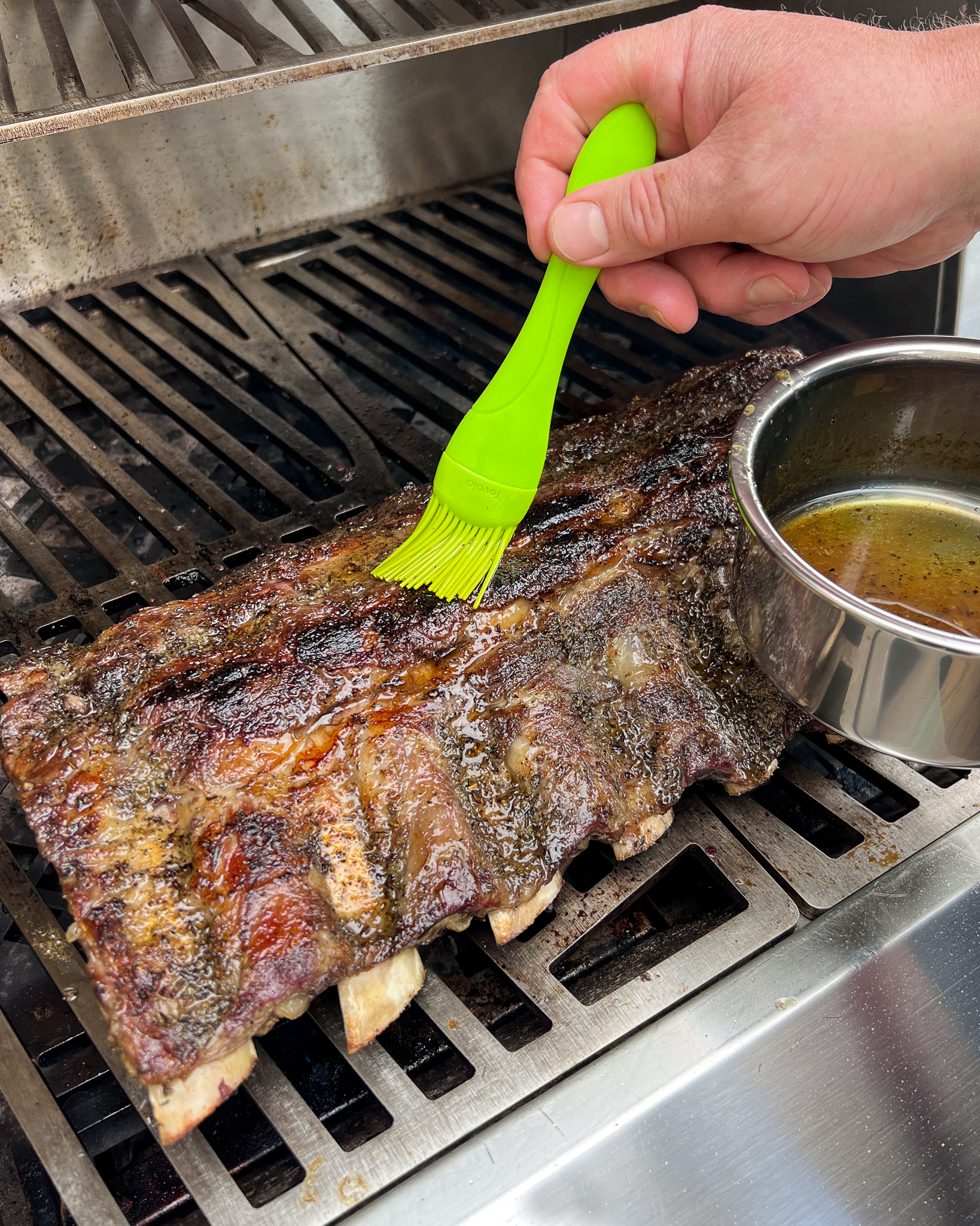 A rack meat being glazed with a brush on a grill.