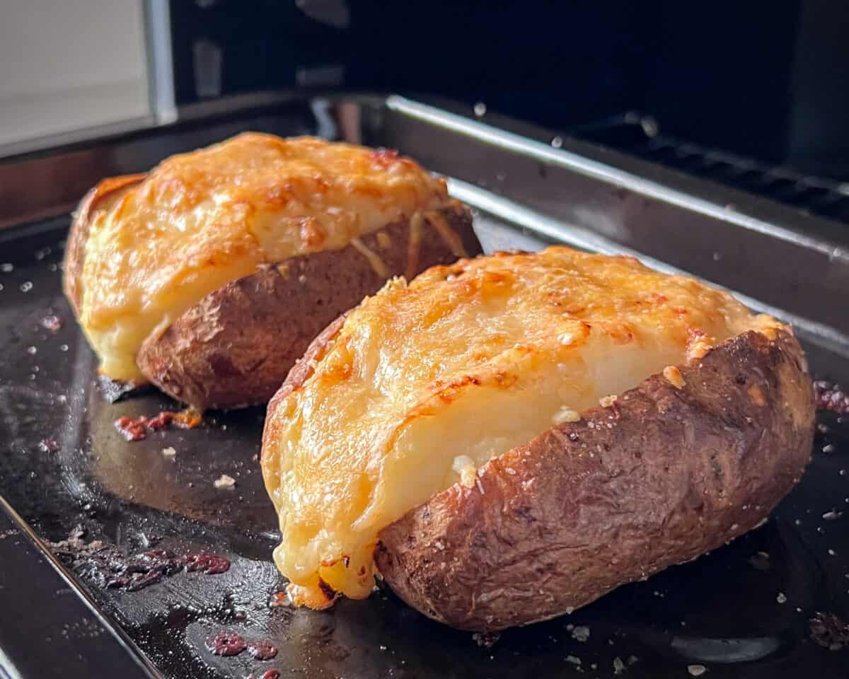 Two finished potatoes with melted cheese coming out of an air fryer.