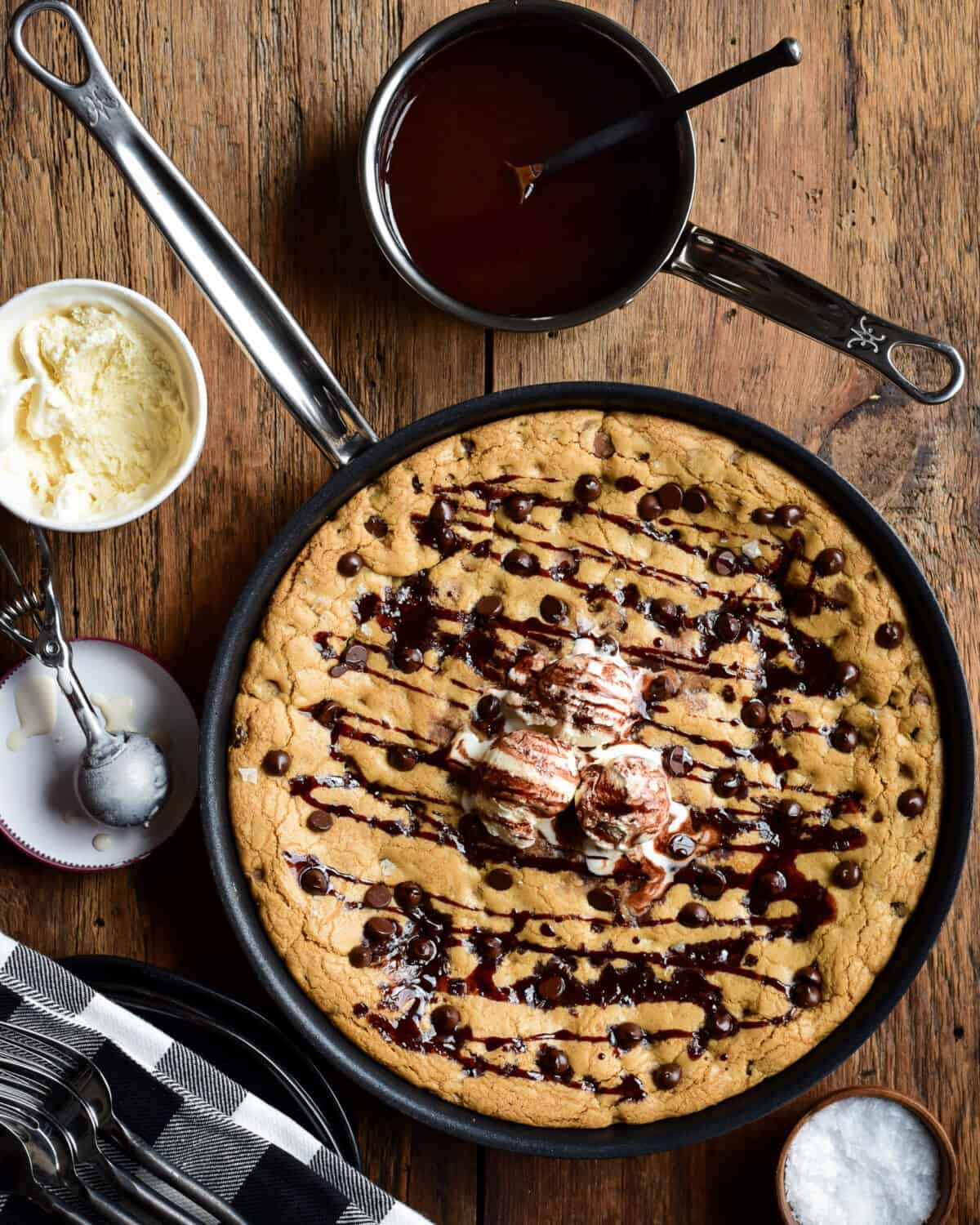 A skillet chocolate chip cookie with ice cream and chocolate sauce drizzle.