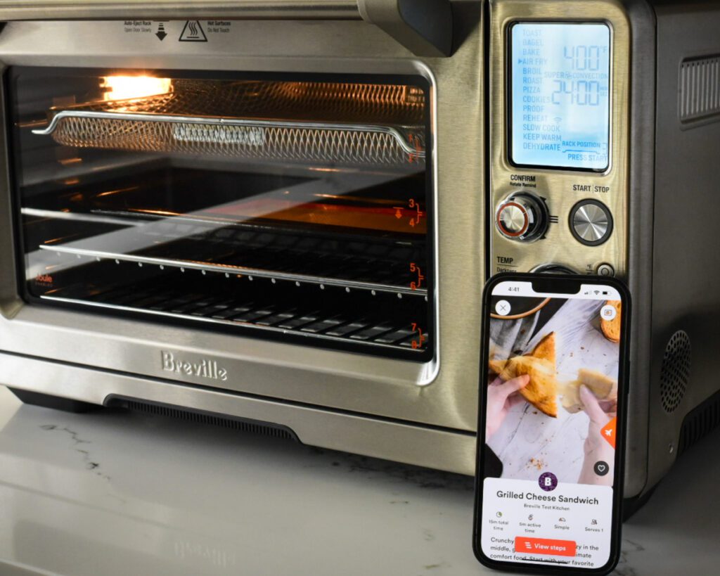 A close up of an air fryer's control panel and an iPhone showing the app.