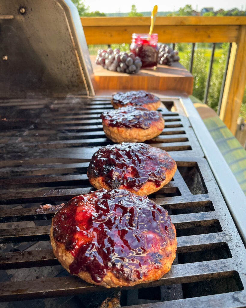 Four burgers stuffed with stilton and glazed with grape jam on the grill.
