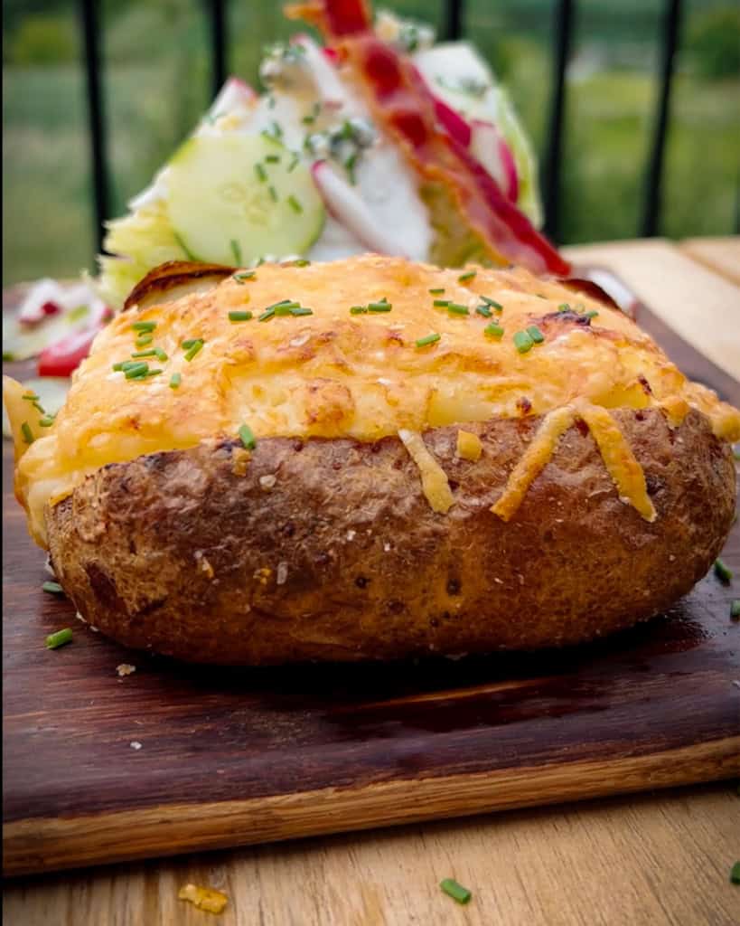 A side view of a baked potato with cheese and chives on the top.
