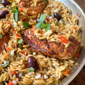A skillet with chicken, orzo, olives and other ingredients.