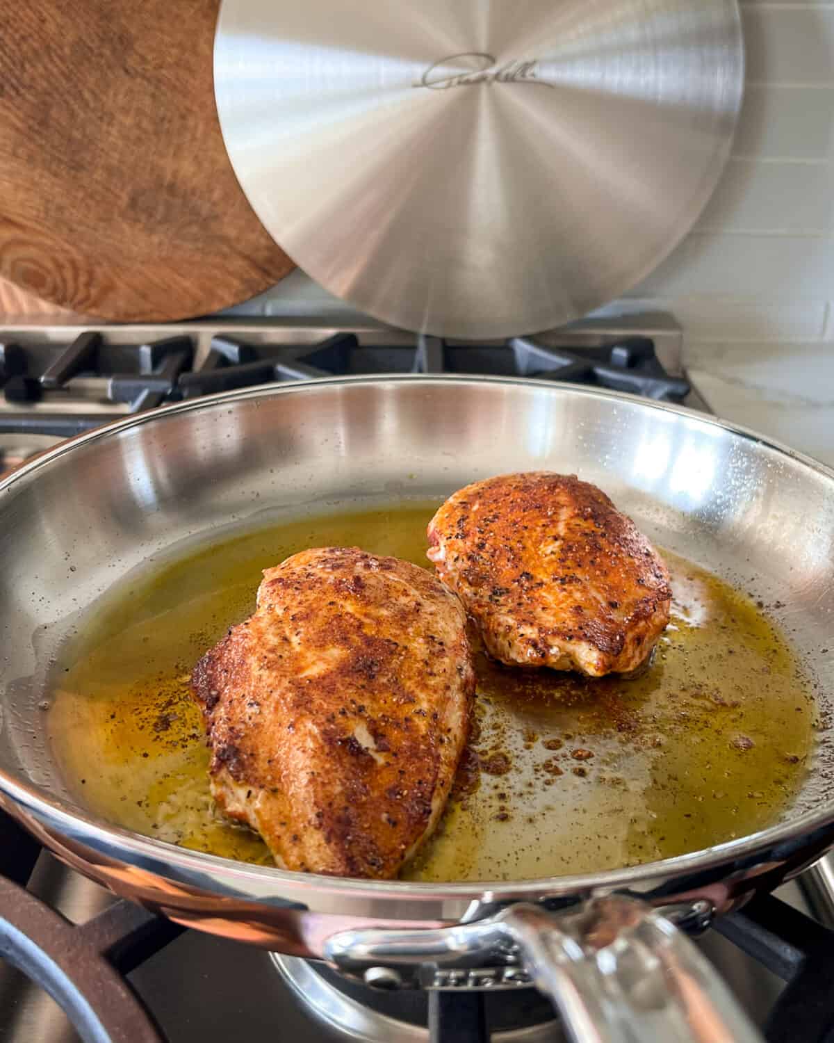 Two seasoned chicken breasts cooking in a skillet,