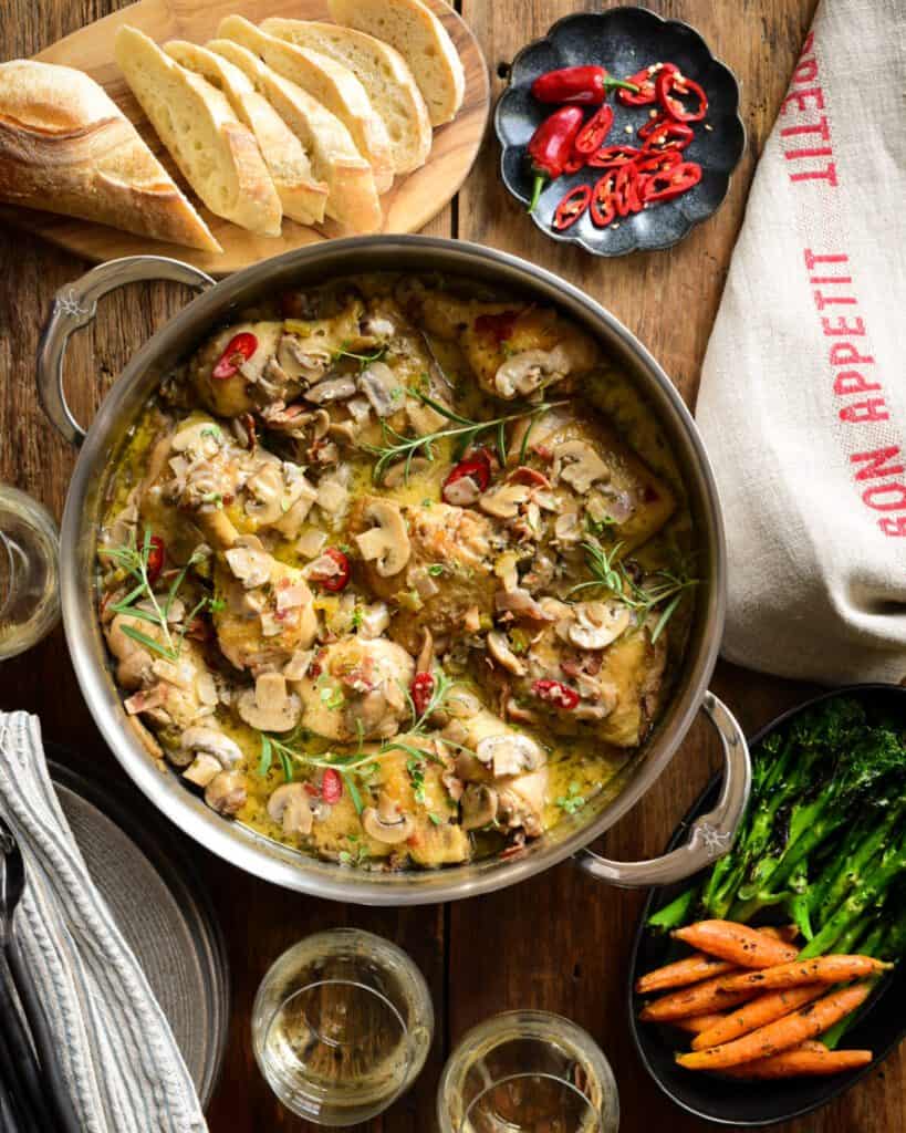 A two handle saucepan with baked chicken in a mushroom white wine sauce.