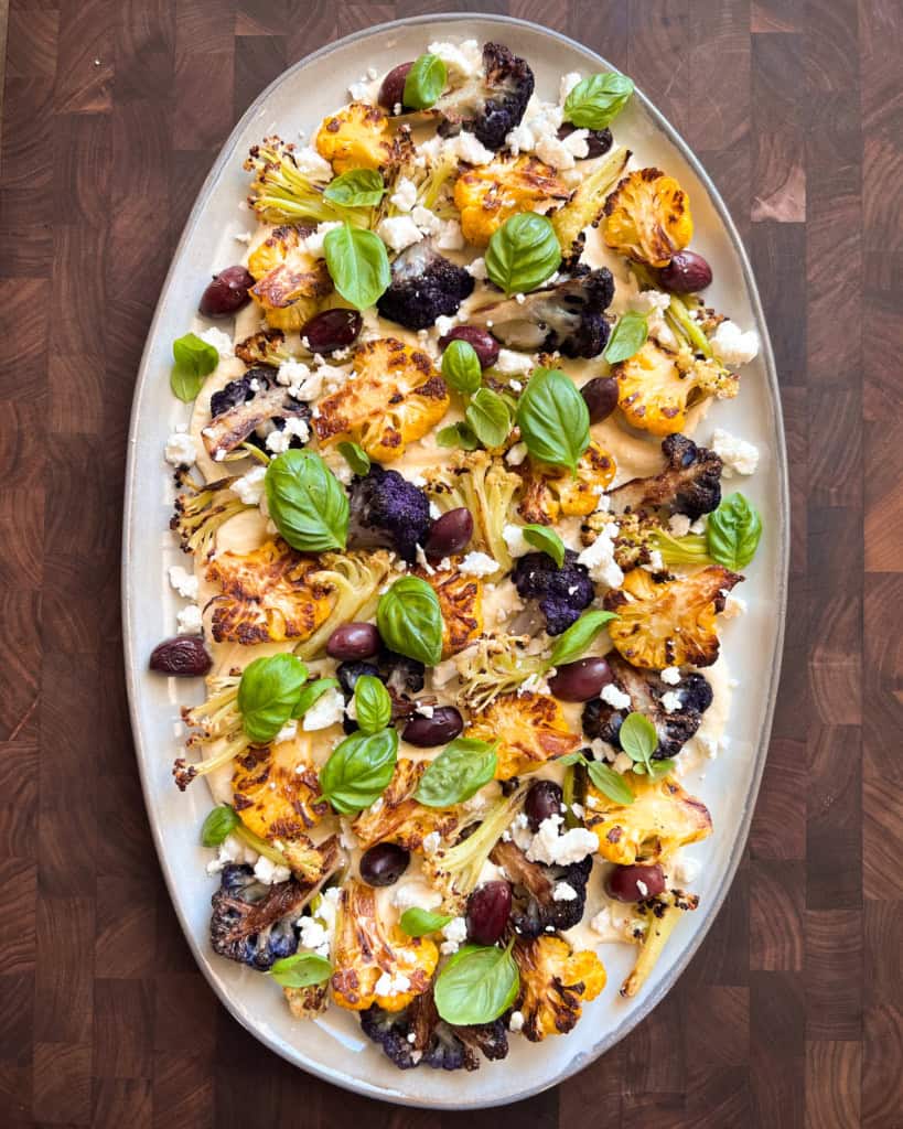 Three varieties of roasted cauliflower and olives on a bed of hummus with basil and feta.