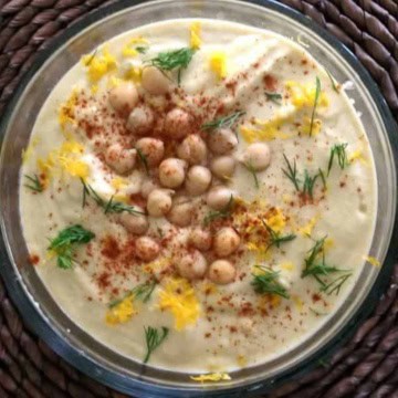 A bowl of hummus with chickpeas and dill.