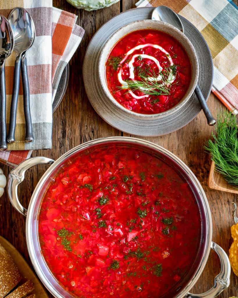 This is a top-down image of a big pot and bowl of borscht topped with a swirl of yogurt and dill on top.