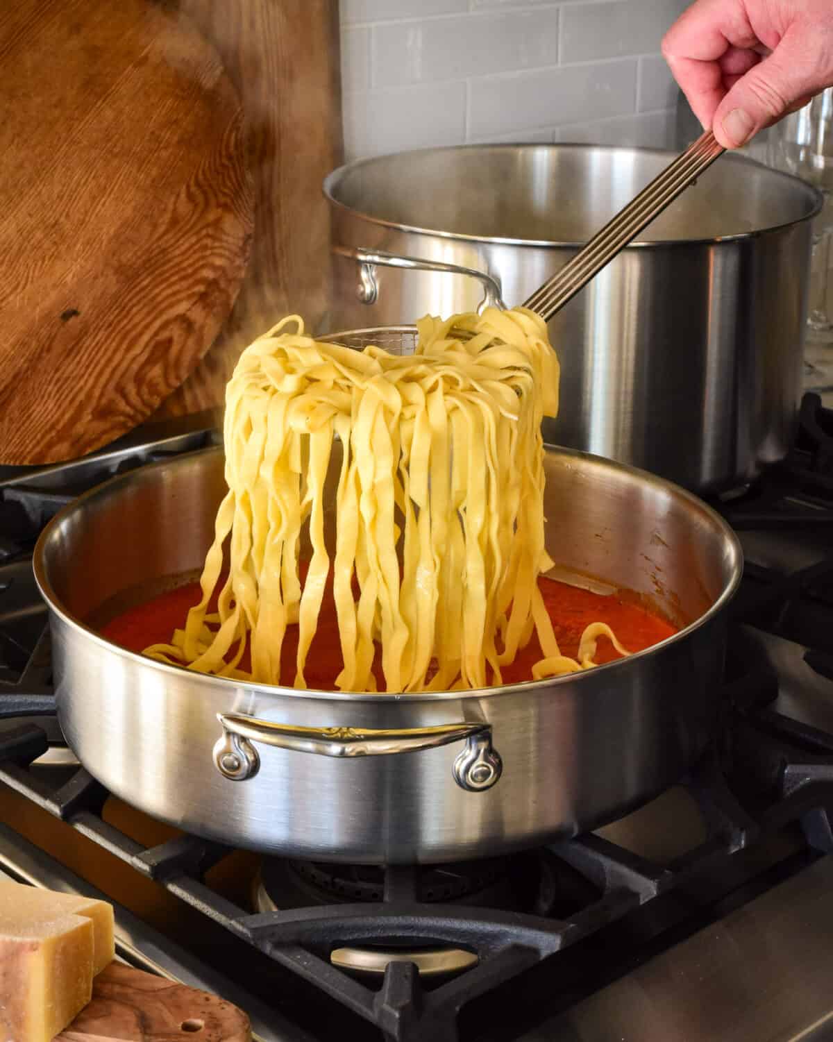Adding pasta noodles into a pan on with a tomato sauce.