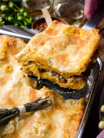 A piece of Butternut Squash and Turkey Sausage Lasagna is being lifted out of a baking pan.