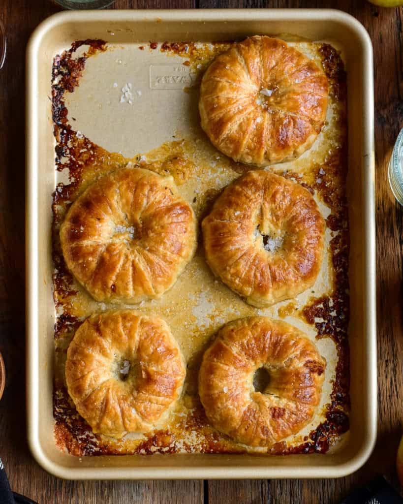 A close up of five donut-like apple pies on a tray.