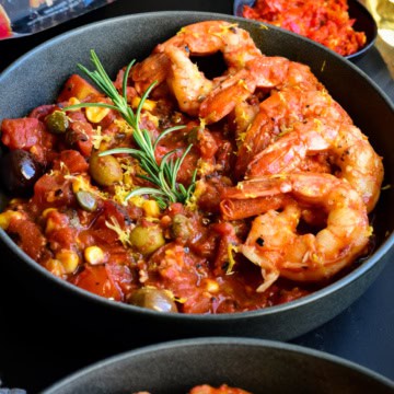A bowl with six colossal shrimp along one side on a base of spicy sauce.