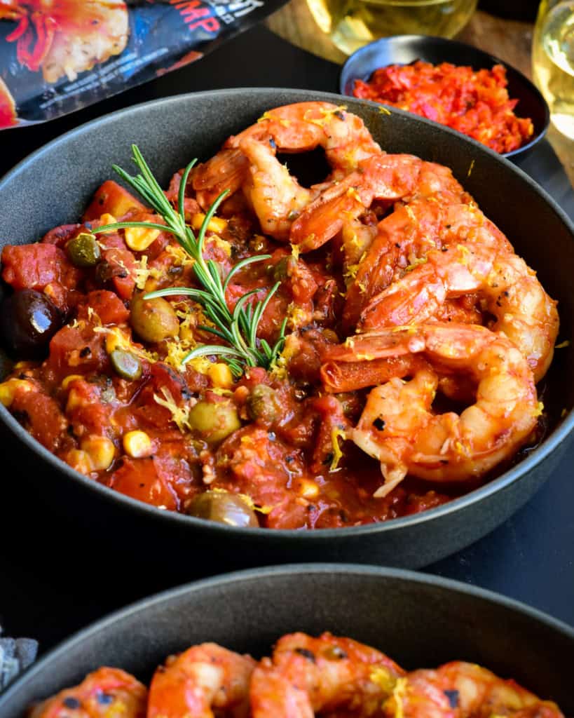 A bowl with six colossal shrimp along one side on a base of spicy sauce.