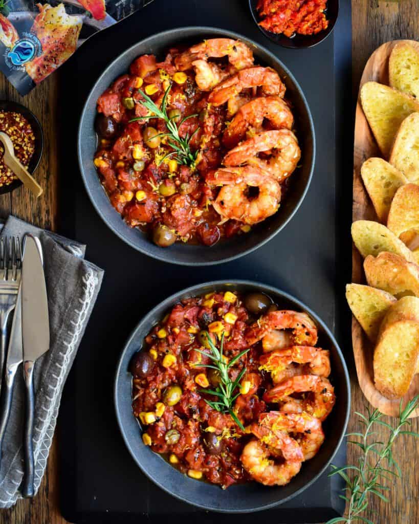 Two bowls with a spicy tomato sauce and five shrimp placed neatly along one side. Served with white wine and toast.