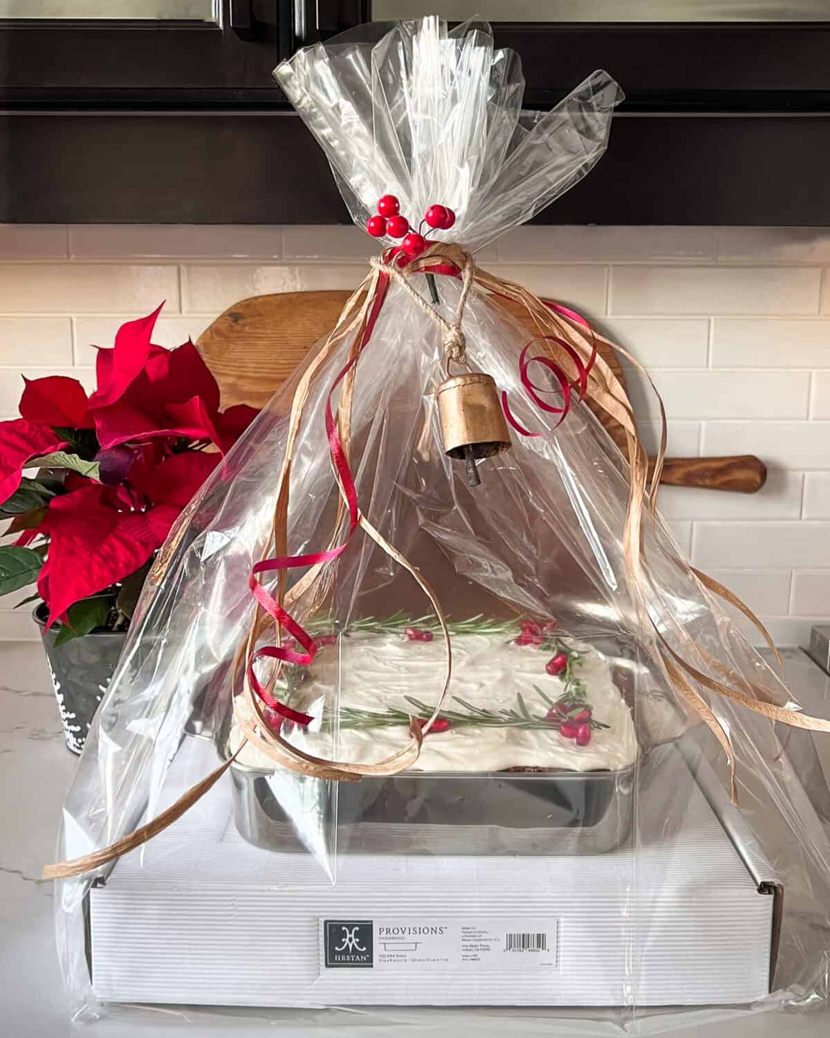 A gift of a carrot cake wrapped in a cellophane bag with ribbon and a bell.