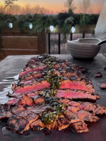 A medium rare and sliced grilled flank steak with herb sauce over the top.