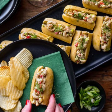 A platter of shrimp rolls with a woman holding one on a plate with chips.