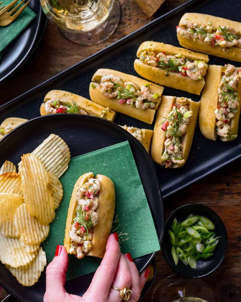 A platter of shrimp rolls with a woman holding one on a plate with chips.