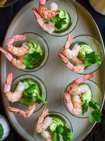 Six individual shrimp cocktails in glass cups with avocado crema.