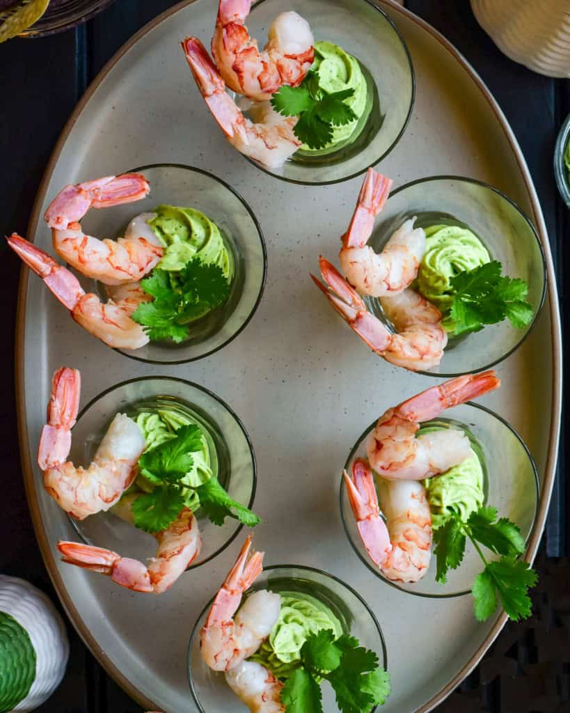 Six individual shrimp cocktails in glass cups with avocado crema.