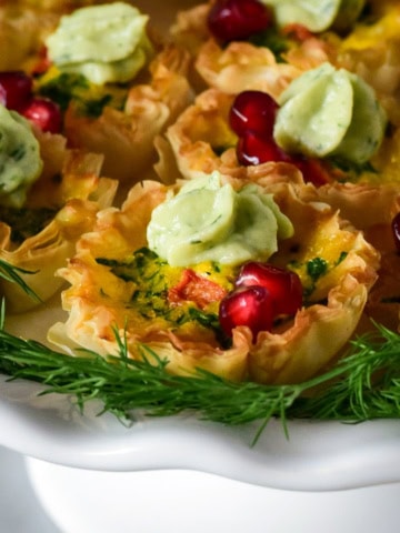 A close up of a festive mini quiche with a crema dollop and arils.