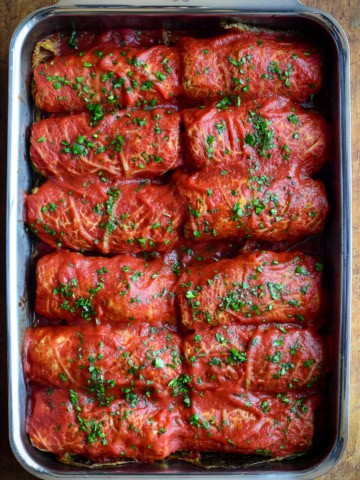 Two rows of cabbage rolls with tomato sauce in a baking pan.