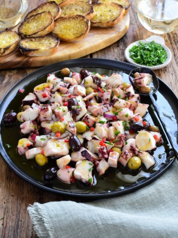 A Marinated Squid Salad with red peppers and olives served with toast and white wine.