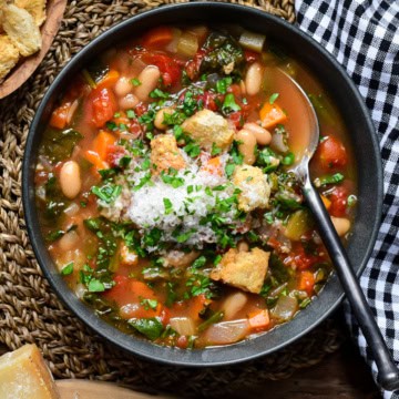 A bowl of rustic vegetable soup with beans, spinach and served with grated Parmesan cheese.