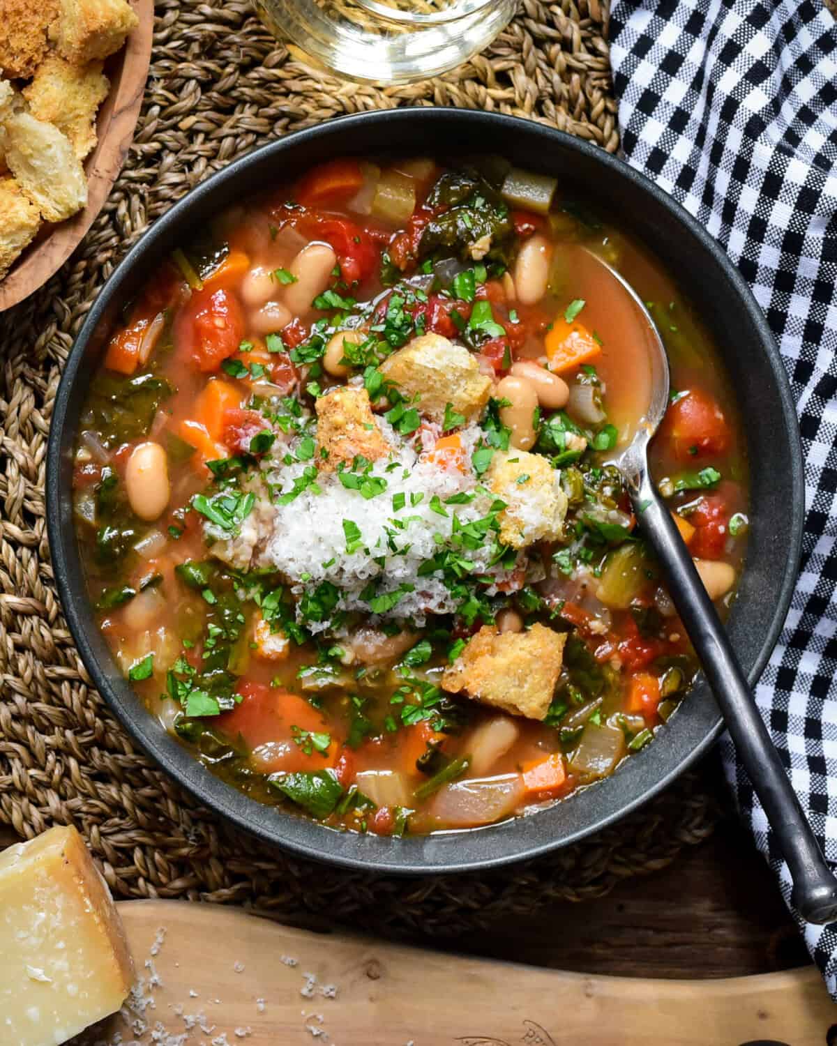 A bowl of rustic vegetable soup with beans, spinach and served with grated Parmesan cheese.