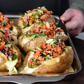 A side view of five large twice cooked baked potatoes on a sheet pan.