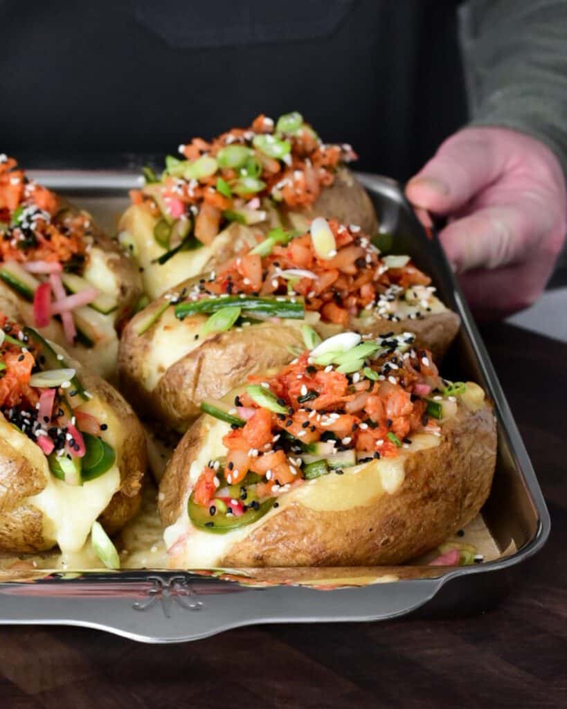 A side view of five large twice cooked baked potatoes on a sheet pan.