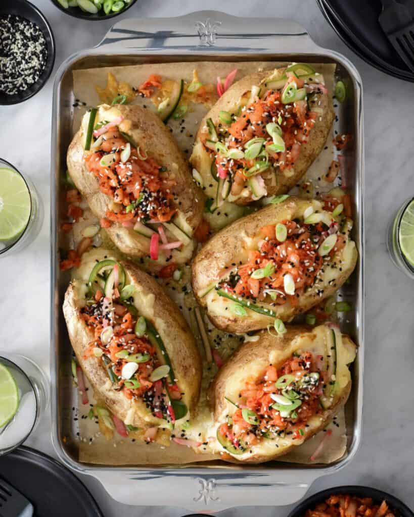 Five Twice-Baked Potatoes topped with Kimchi and pickled veggies on a sheet pan.
