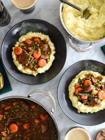 Two bowls and a pot of Guinness and Beef stew served with with mashed potatoes.