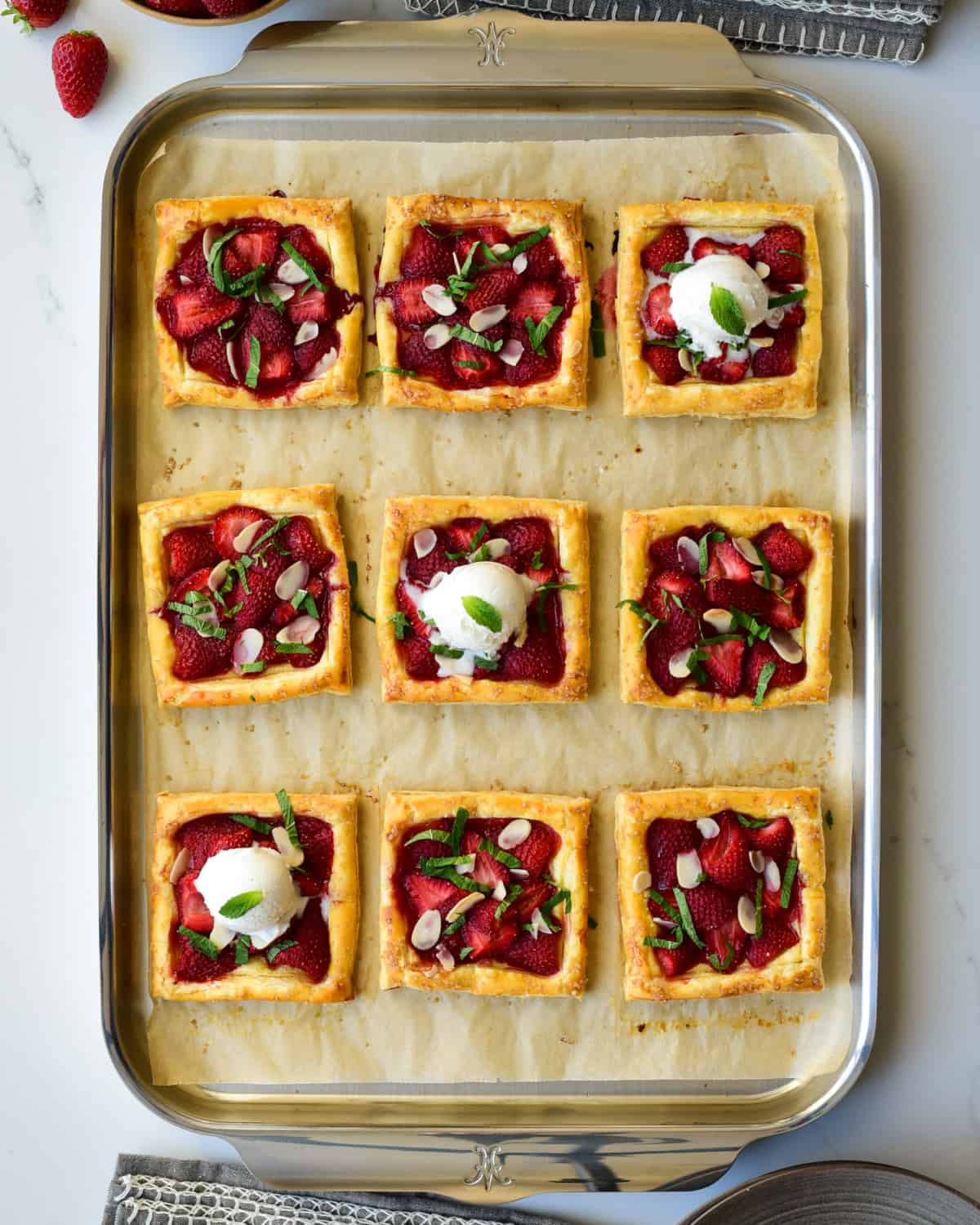 Nine Puff Pastry Strawberry Tarts on a sheet pan, served with a scoop of ice cream.