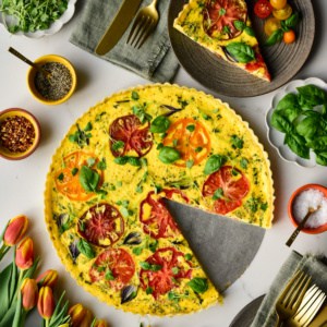 An heirloom tomato onion quiche with a slice removed and placed on a side plate.
