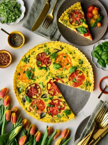 An heirloom tomato & pearl onion quiche with a slice removed and served with a fresh tomato salad.