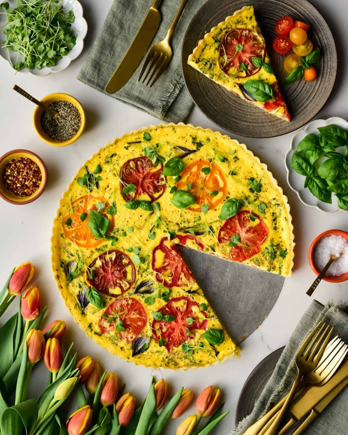 An heirloom tomato & pearl onion quiche with a slice removed and served with a fresh tomato salad.