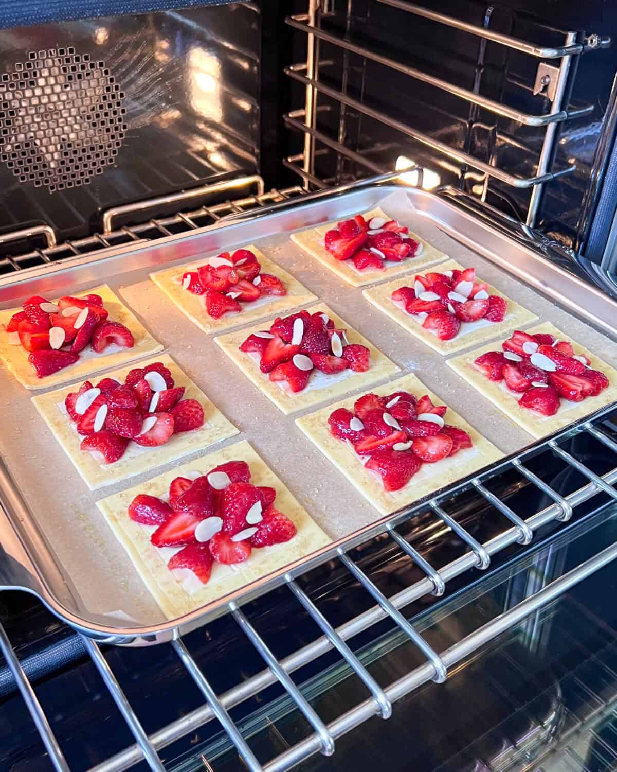 A sheet pan with nine Puff Pastry Strawberry Tarts going into the oven.