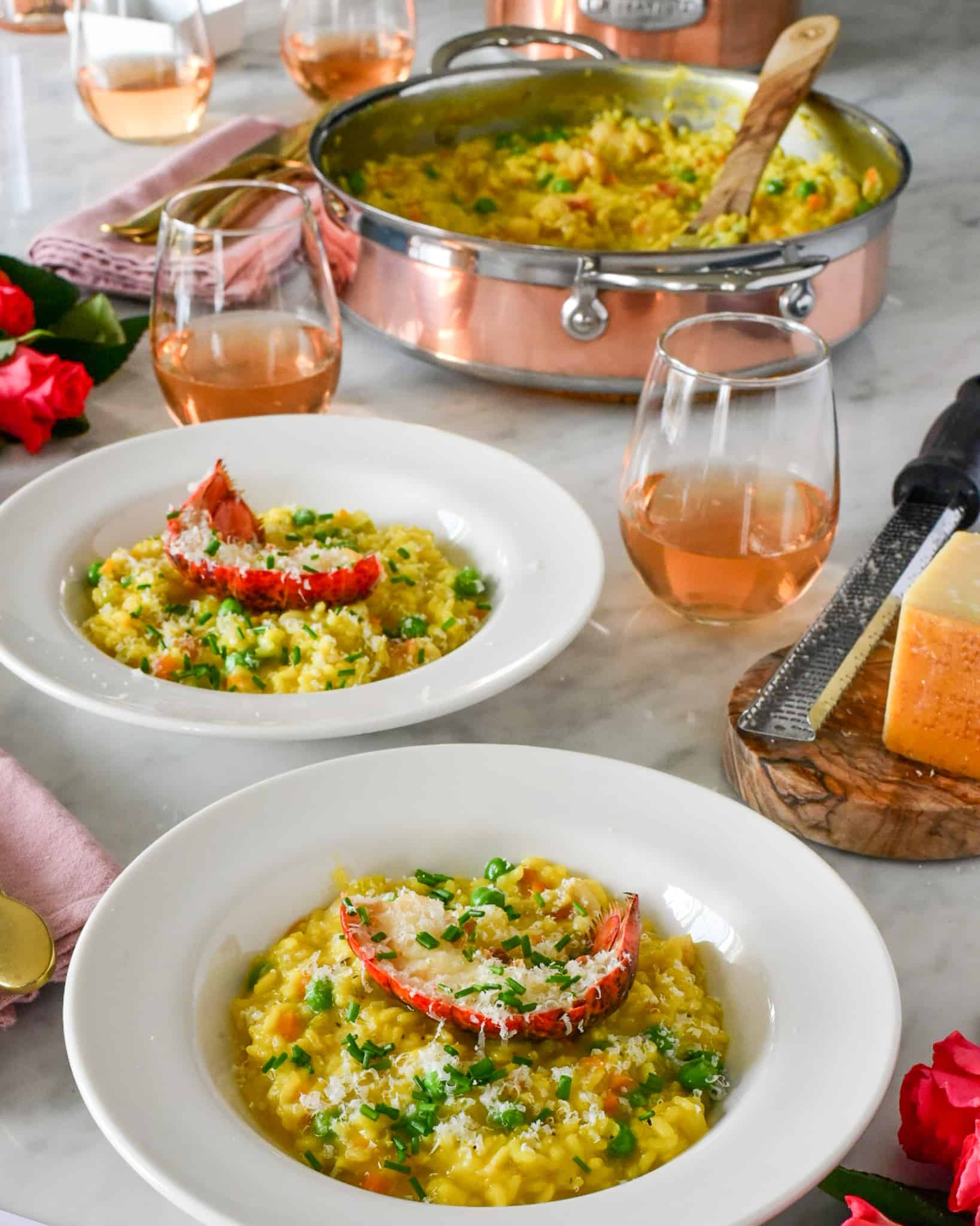 Two bowls of lobster tail risotto with a copper pan in the background with risotto.