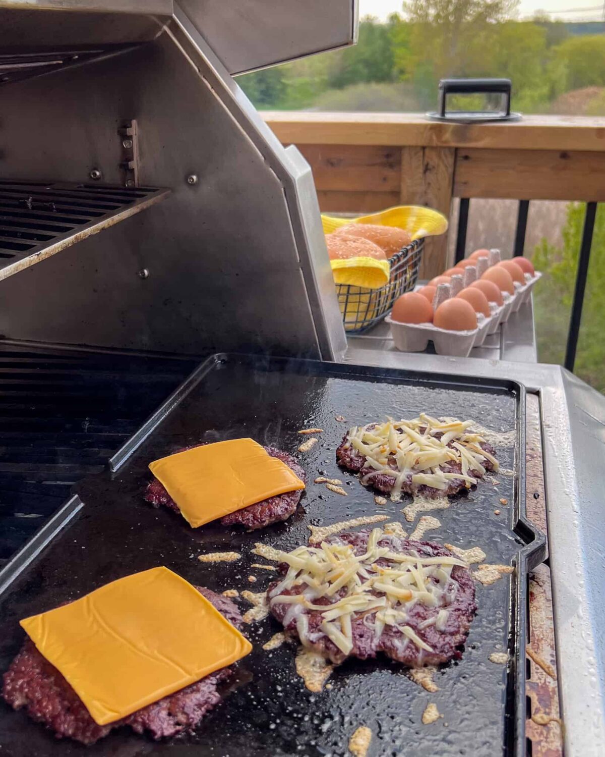 Four smash burgers on the griddle with two types of cheese.