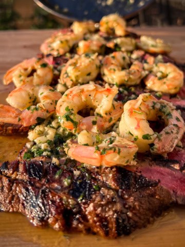 A grilled flank steak topped with garlic shrimp.