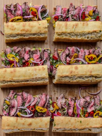 Six grilled steak sandwiches on baguettes.